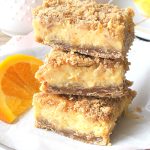 3 crumbs bars are piled on a white parchment paper with an orange slice on the side.