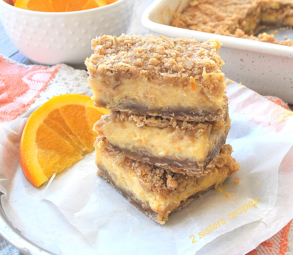 3 orange bars piled on a plate with wax paper and a slice of orange.  by 2sistersrecipes.com