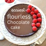 A round chocolate cake served on a cake platter with fresh raspberries on top.