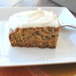 A slice of carrot cake with white frosting on top, on a white plate.