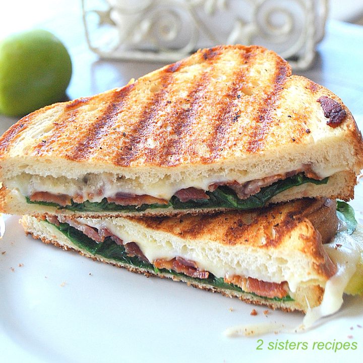 A grilled sandwich sliced in half and placed on top of each other served on a white plate.