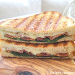 A sandwich cut in half and sittinig on a wood board. by 2sistersrecipes.com