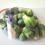A net filled with Brussels Sprouts on a white cutting board.