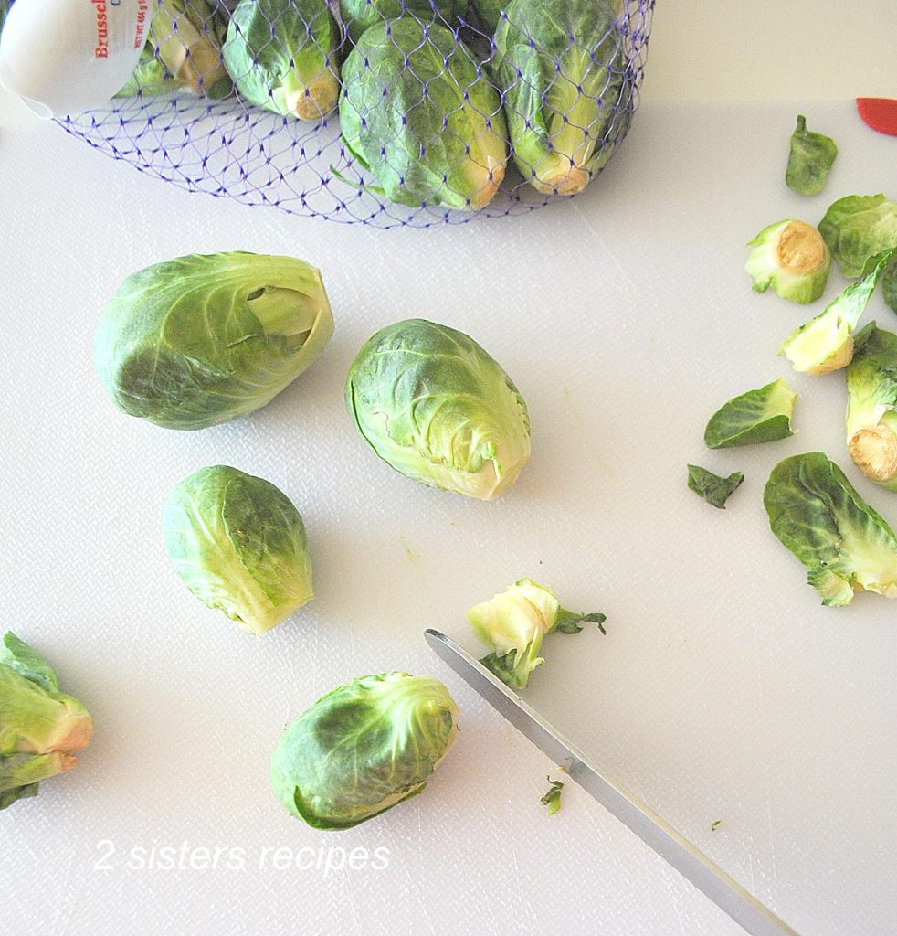On a white cutting board, cutting the end of the Brussels sprouts. by 2sistersrecipes.com