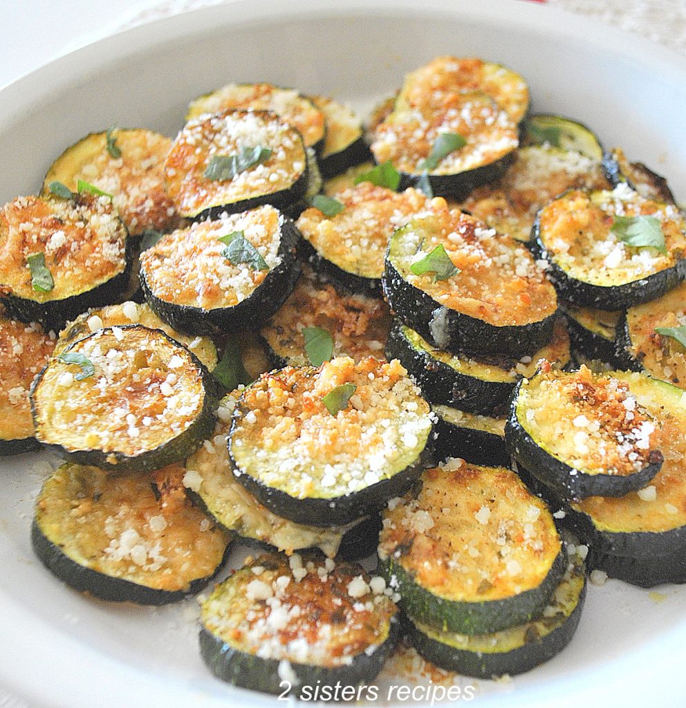Roasted Pamesan Zucchini in a white serving dish. by 2sistersrecipes.com