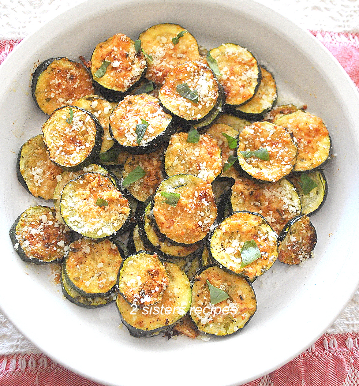 A white plate filled with Zucchini disks roasted and topped with grated cheese.