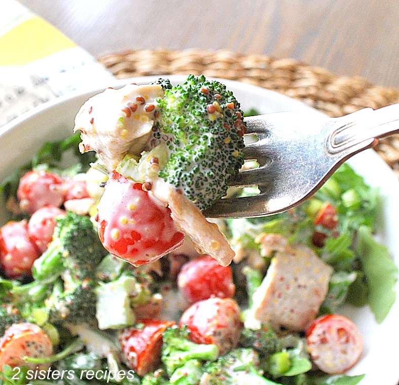 A forkful of broccoli, chicken and cherry tomato from a bowl of salad.