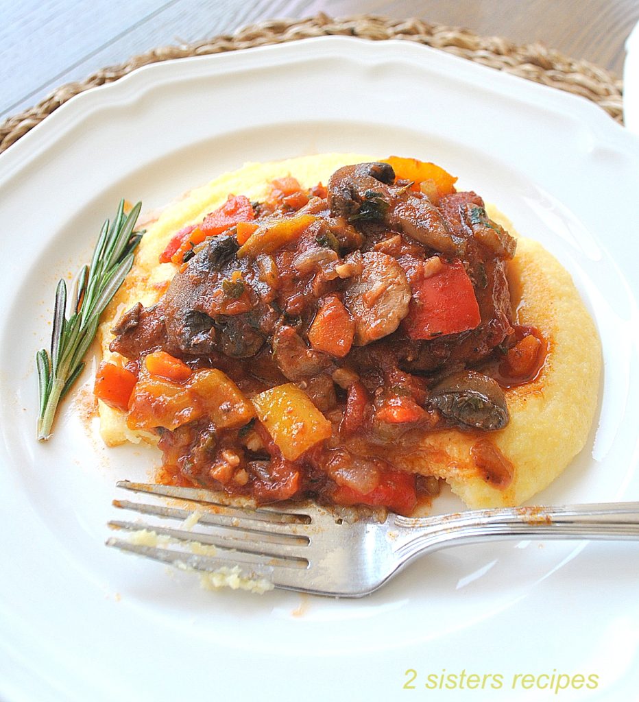 On white plate, a layer of polenta with chicken cacciatore on top. by 2sistersrecipes.com