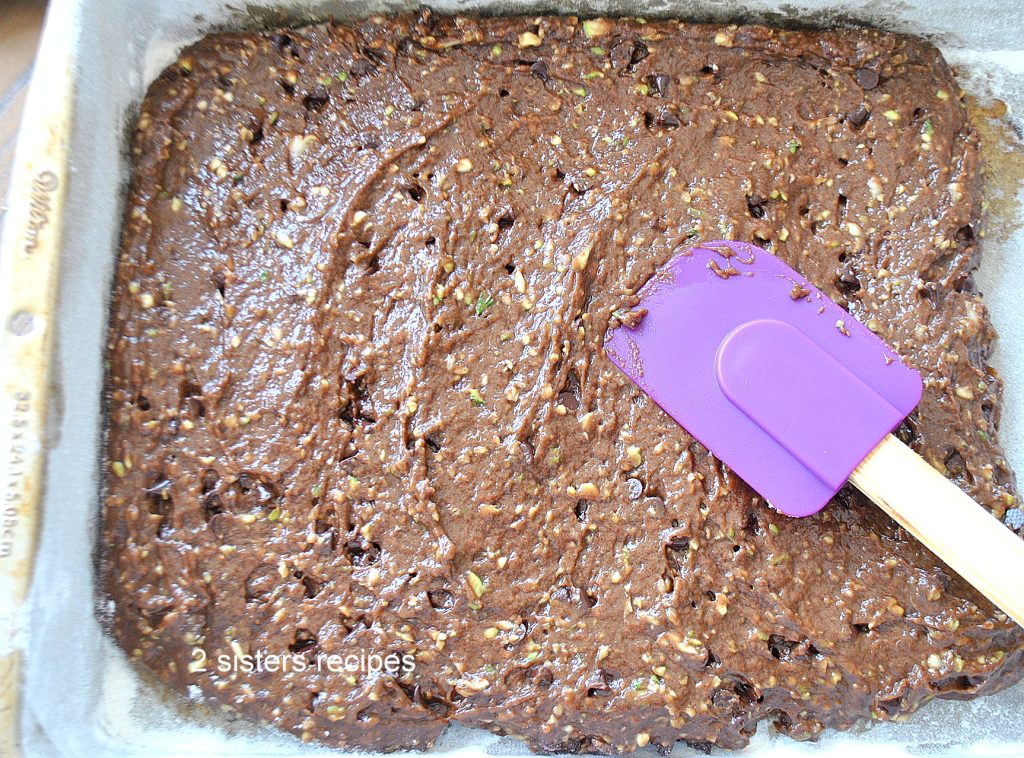 Spreading the brownie batter in a baking pan with a purple spatula. 