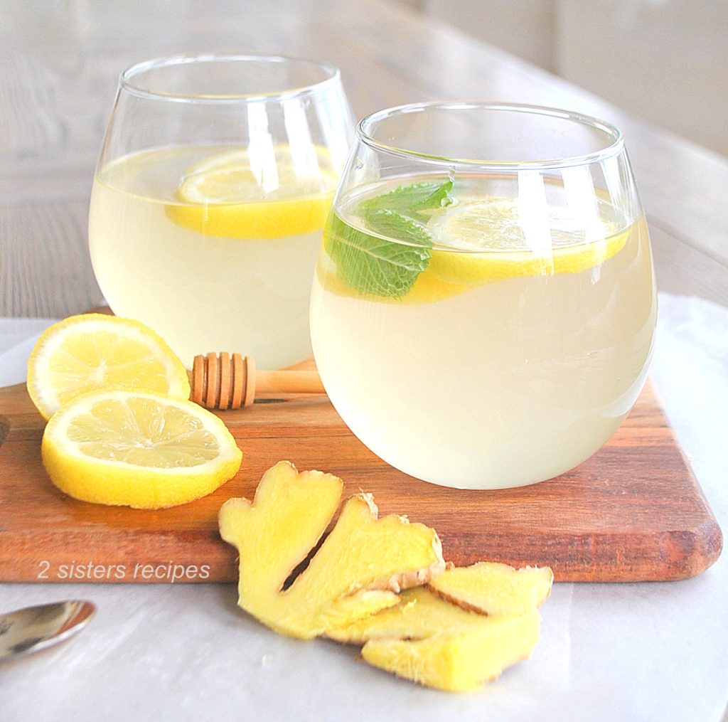 Two glasses filled with Lemon Ginger Honey Water on a wood board.