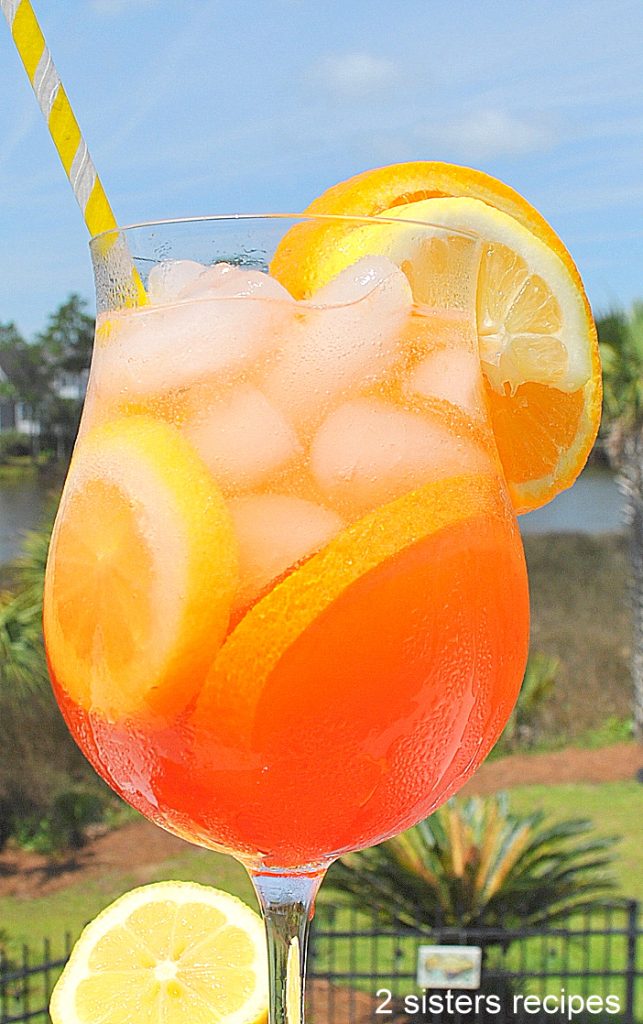 A close up photo of an orange colored cocktail, set on the ledge of outside. by 2sistersrecipes.com