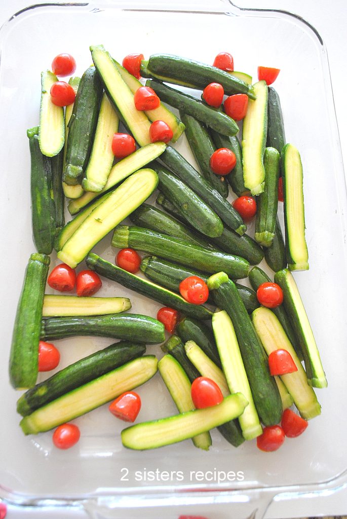 Raw mini zucchini and cherry tomatoes tossed in glass Pyrex baking dish. by 2sistersrecipes.com