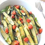 An oval white platter filled with baby zucchini and cherry tomatoes.