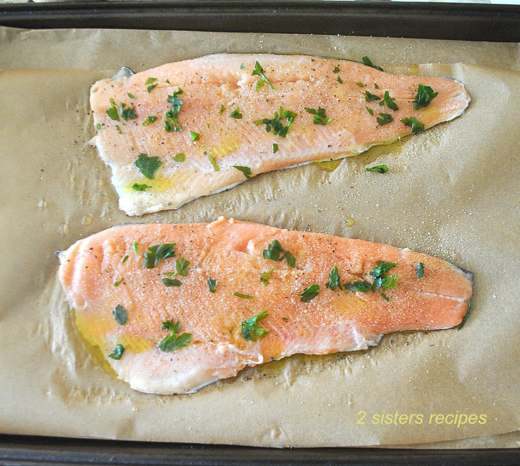 Raw Trout is place on parchment paper on a baking pan and seasoned  with seasonings and herbs. by 2sistersrecipes.com
