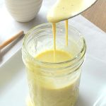 A spoonful of honey mustard dressing is poured back into a mason jar.