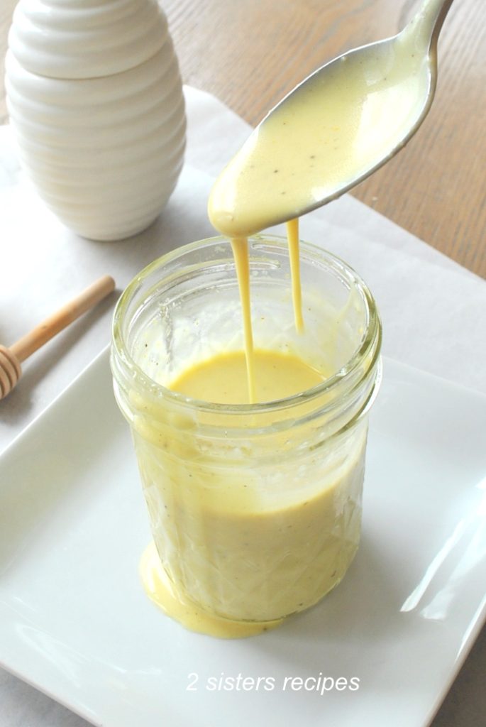 A spoon dripping the soft yellow mustard dressing back into the jar. 