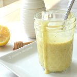 A small mason jar with honey mustard dressing and a spoon inside.