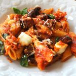 A dish with penne pasta with cubes of roasted eggplants and mozzarella cheese.