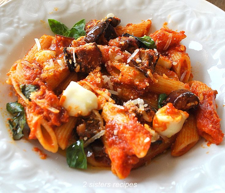 A dish with penne pasta with cubes of roasted eggplants and mozzarella cheese.