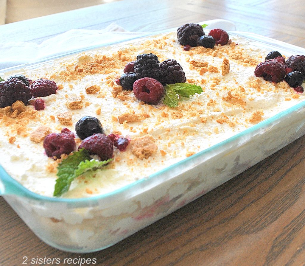 a glass baking dish filled with whipped cream and topped with frozen mixed berries.
