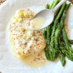 Spooning the lemon-dijon sauce over the baked cod, with asparagus on the side.
