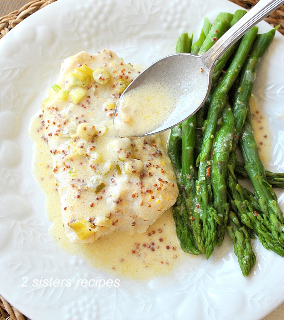Spooning the lemon-dijon sauce over the baked cod, with asparagus on the side.