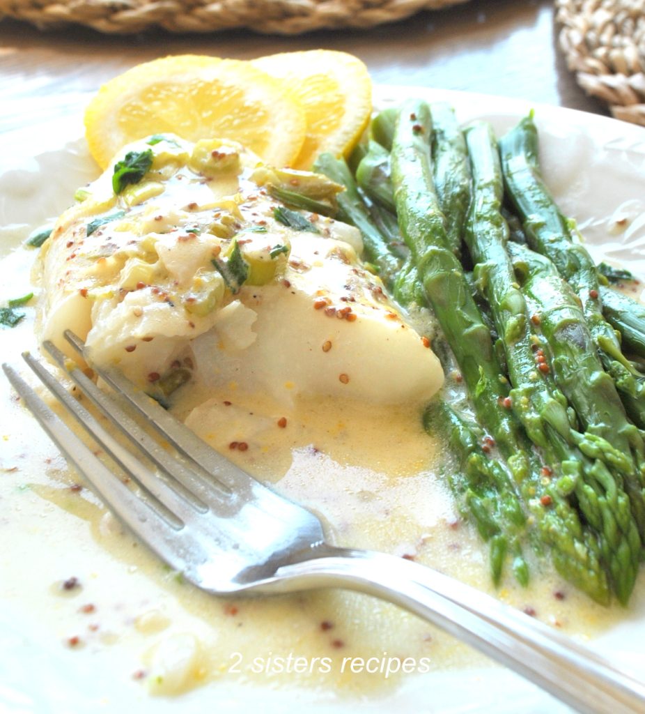 Cod fish in a white plate and fork and asparagus on the plate. by 2sistersrecipes.com