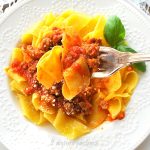 A forkful of Sausage Ragu served with pappardelle pasta in a white plate.