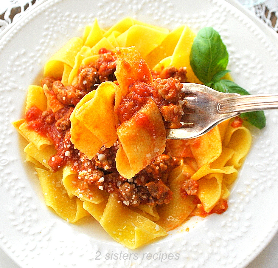  A forkful of Sausage Ragu served with pappardelle pasta in a white plate.