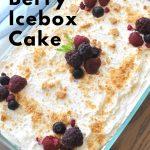 A glass baking dish filled with whipped cream and mixed berries on top, with scatter crumbs.