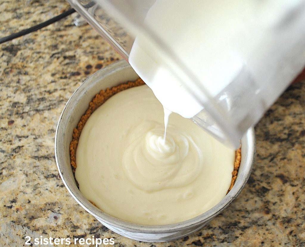 Pouring the first layer of cheesecake mixture over the crust in a springform cake pan. by 2sistersrecipes.com