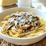 A white bowl filled with wide noodle pasta topped with mushrooms ragu and grated cheese.