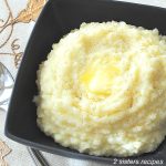 A black bowl, square shaped - filled with mashed potatoes will slice of butter on top.