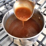 A ladle pouring some brown gravy back into a sauce pan.