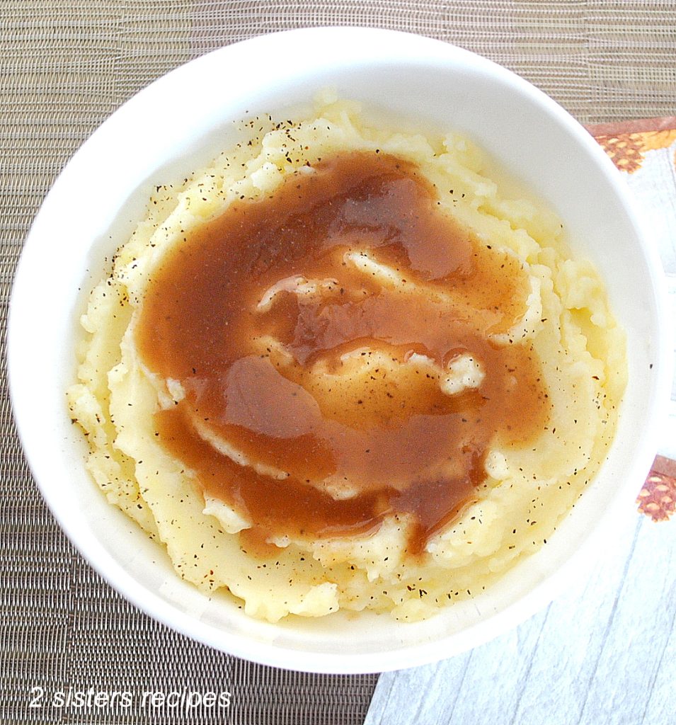 A white bowl filled with creamy mashed potatoes and some brown gravy on top. by 2sistersrecipes.com