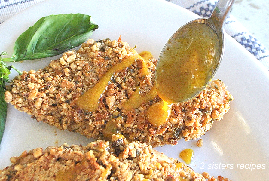 A spoon full of honey mustard sauce is drizzled over the baked nut-crusted chicken. by 2sistersrecipes.com