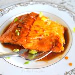 A forkful of salmon glazed with a sauce and scallions on top.