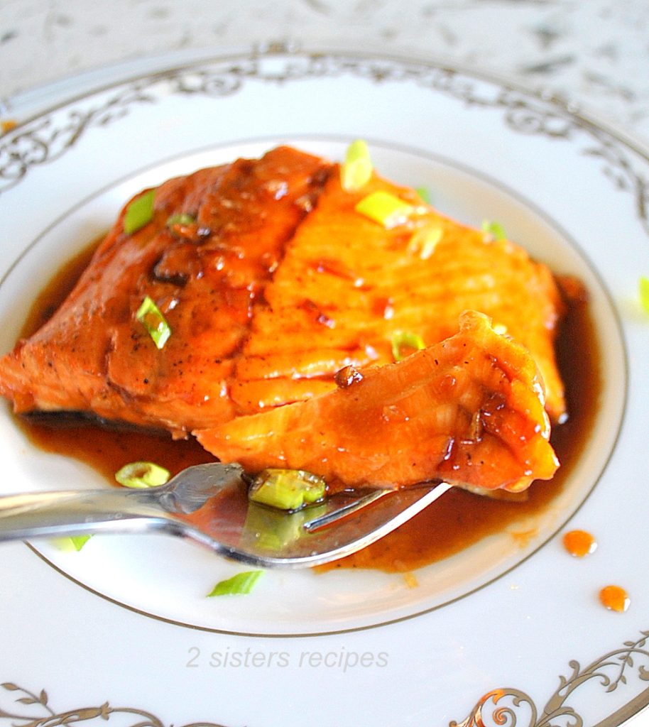 A forkful of salmon glazed with a sauce and scallions on top.