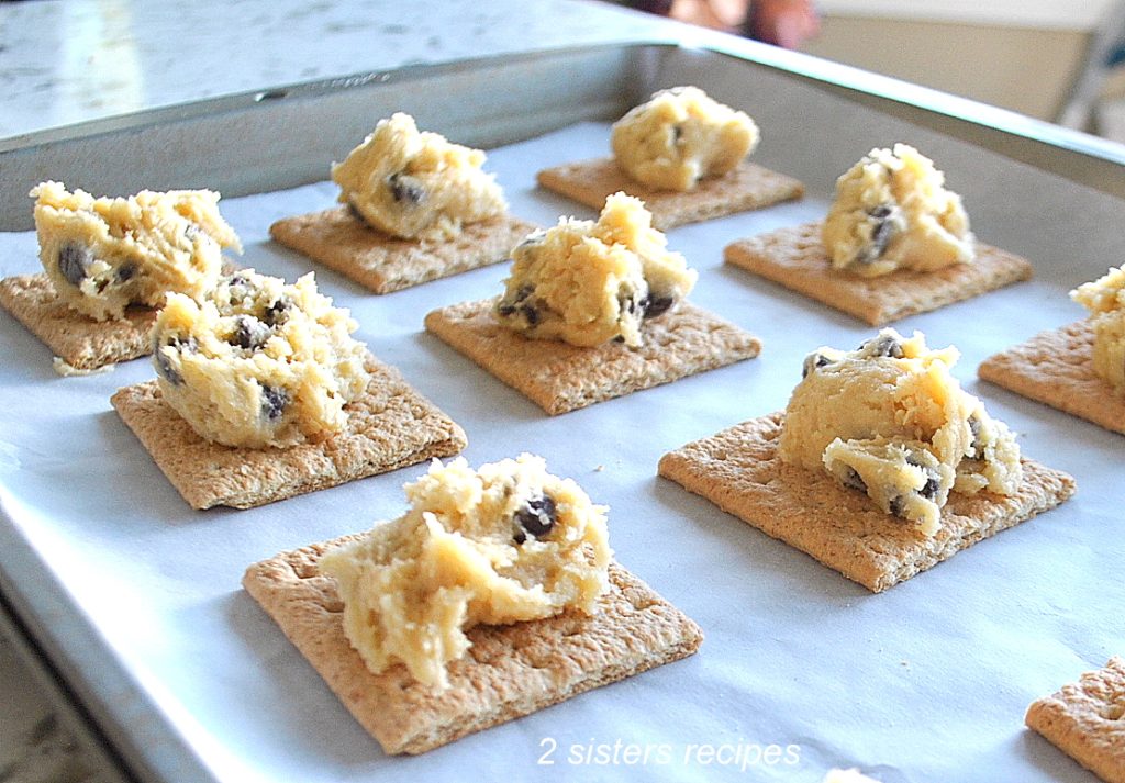On a cookie sheet, graham crackers are topped with chocolate chip cookies dough. by 2sistersrecipes.com 