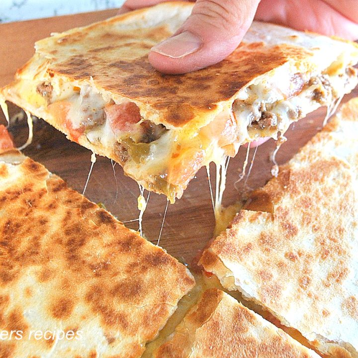 A piece of quesadilla sliced in quarters on a wood cutting board.