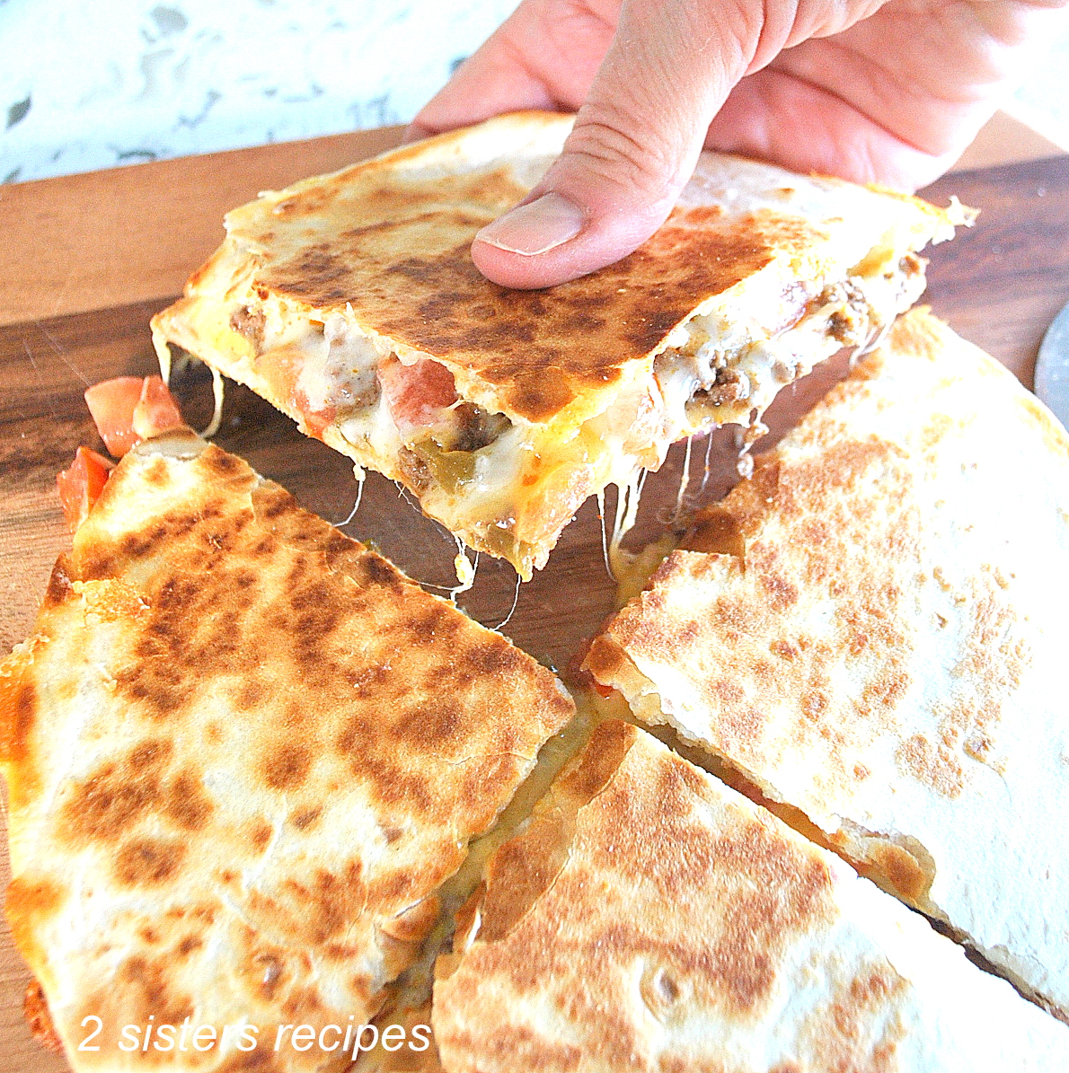 A hand is picking up a piece of loaded quesadilla. by 2sistersrecipes.com