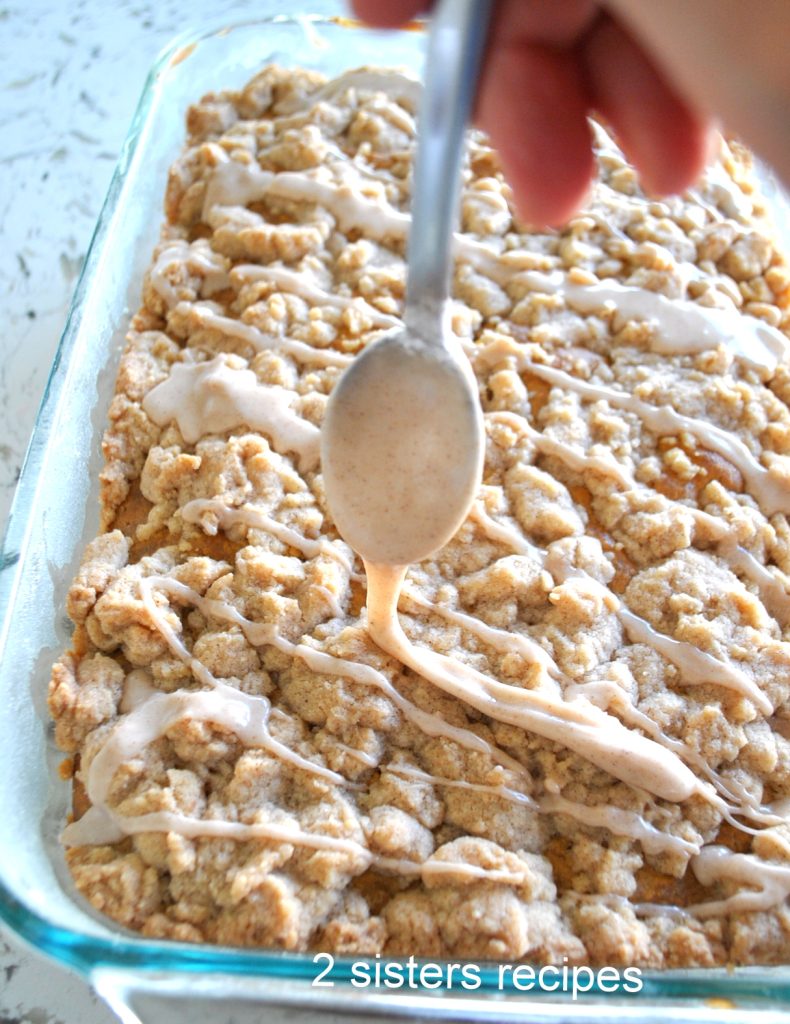 Drizzling cinnamon glaze over the baked Pumpkin Crumb Cake by 2sistersrecipes.com