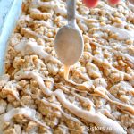 A sheet cake topped with a thick crumb and a spoon with a cinnamon glaze.