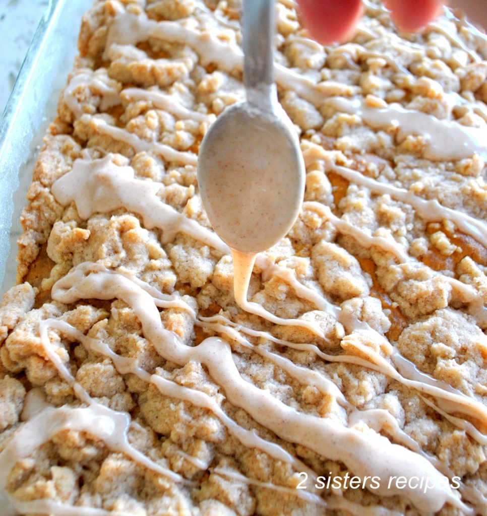 A sheet cake topped with a thick crumb and a spoon with a cinnamon glaze.