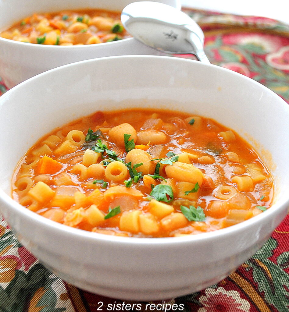 A white bowl of soup in a thick tomato broth with beans and small pasta.