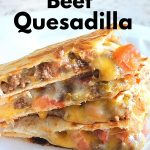 Triangle cut pieces of quesadilla loaded with meat, cheese and veggies served on a white plate.