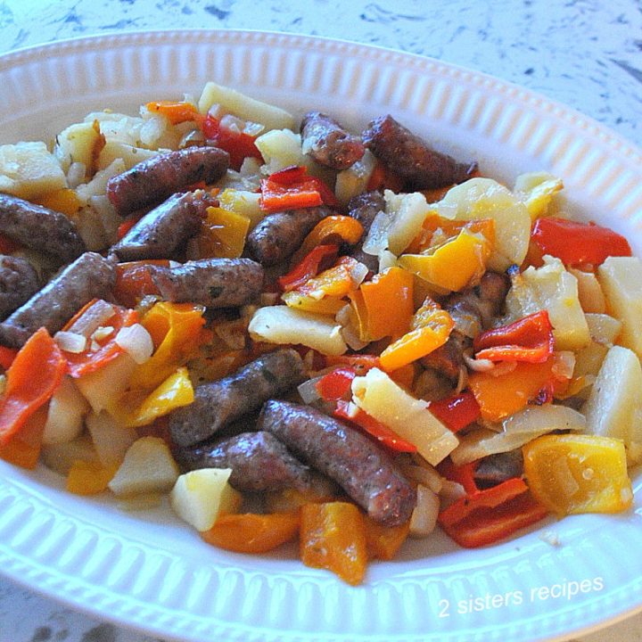 Thin Sausages with peppers and potatoes are served on a large white oval platter.