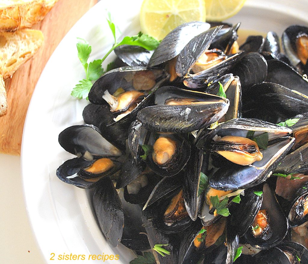 Steamed Mussels in a flavorful garlic fennel broth served in a round white bowl with lemon slices on the side.