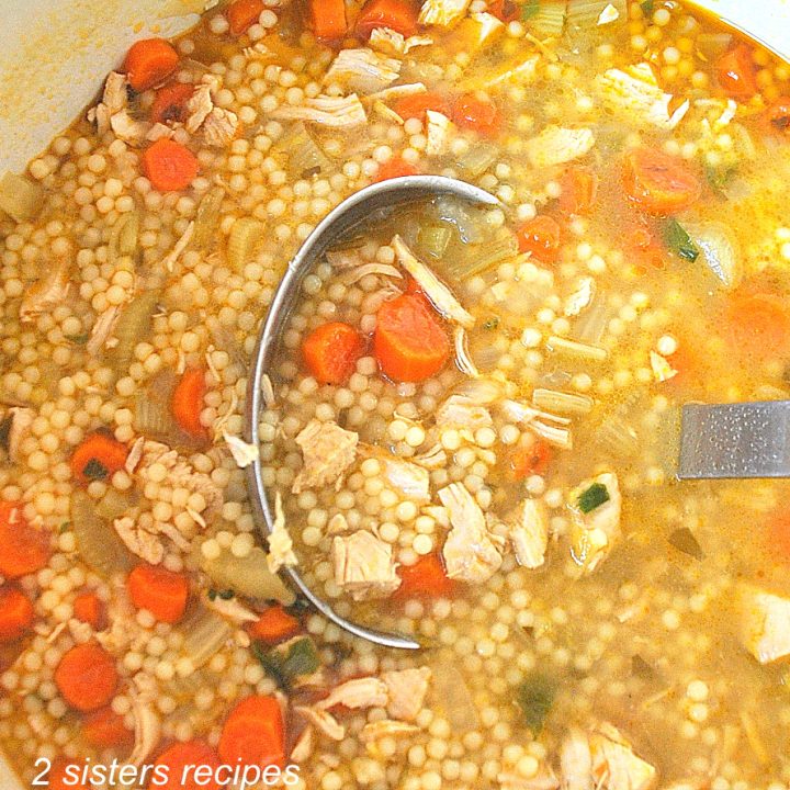 A ladle filled with chicken soup and chopped carrots.