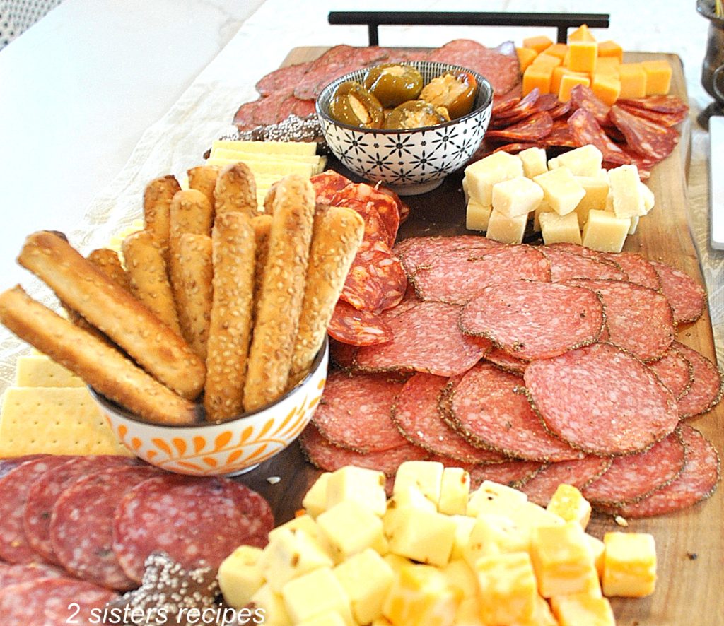 A charcuterie board filled with meats, cheeses, bread sticks and olives,